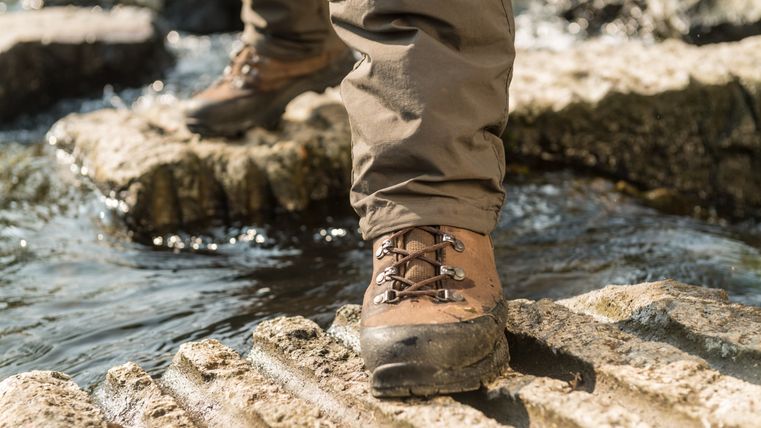 Nahaufnahme eines Wanderstiefels auf einem Felsen über einem fließenden Bach.
