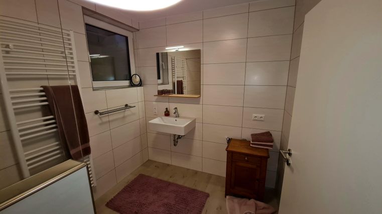 A modern bathroom with bright tiles and a sink. There is a large mirror and a small wooden dresser.