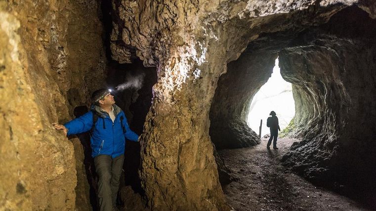 Zwei Personen in der Buchenlochhöhle. Eine trägt eine Stirnlampe und erkundet die Felswände, die andere steht im Höhleneingang.