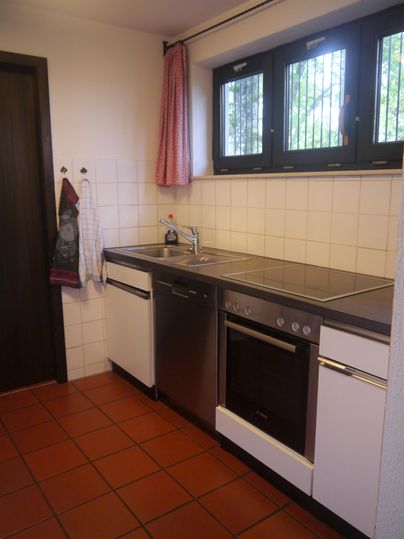 Eine moderne Küche mit weißen und metallischen Oberflächen. Es gibt ein Waschbecken, einen Herd und Fenster mit Blick nach draußen.