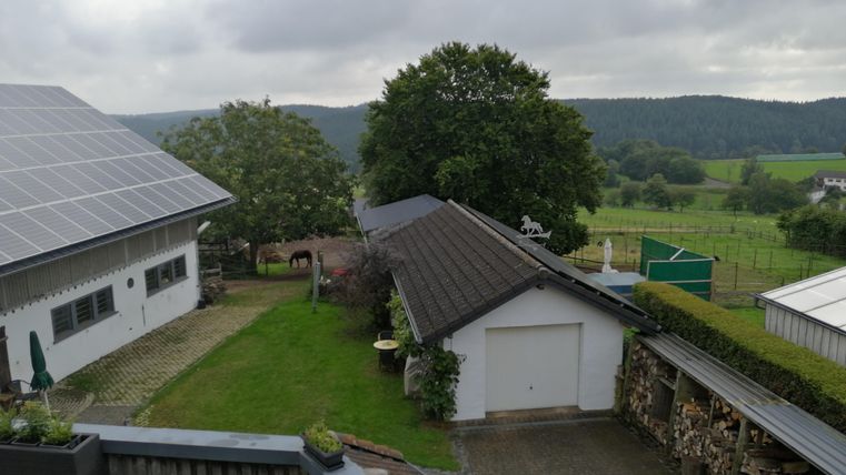 Een landelijke uitzichten met een nette tuin en meerdere gebouwen. Op de achtergrond zijn zachte heuvels en bomen te zien.