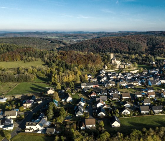 Luftaufnahme von Kerpen mit Burg in der Mitte, umgeben von Häusern und grüner Landschaft unter blauem Himmel., © Eifel Tourismus GmbH, D. Ketz