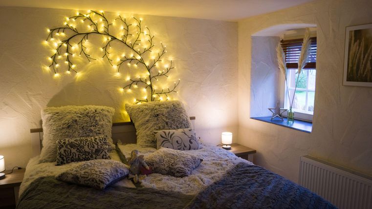 Een gezellig slaapkamer met een groot bed en zachte kussens. Aan de muur straalt een decoratieve lamp in de vorm van een boom.