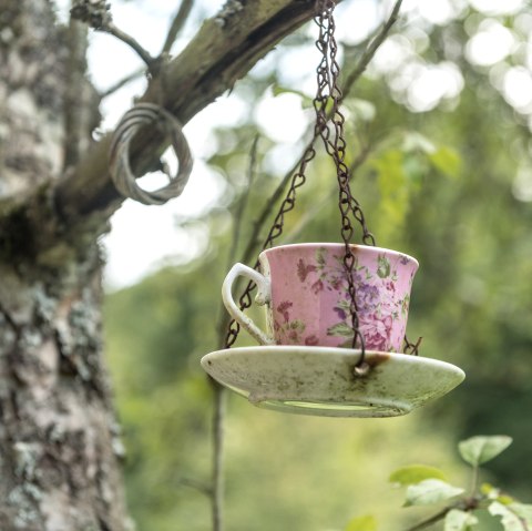 Eine rosa Tasse mit Blumenmuster hängt an einer Kette an einem Ast in einem grünen, bewaldeten Umfeld., © Eifel Tourismus GmbH, Dominik Ketz