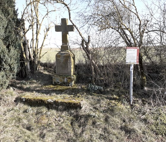 A stone wayside cross near Auel, surrounded by trees and an information board, stands in a meadow., © Touristik GmbH Gerolsteiner Land, Ute Klinkhammer