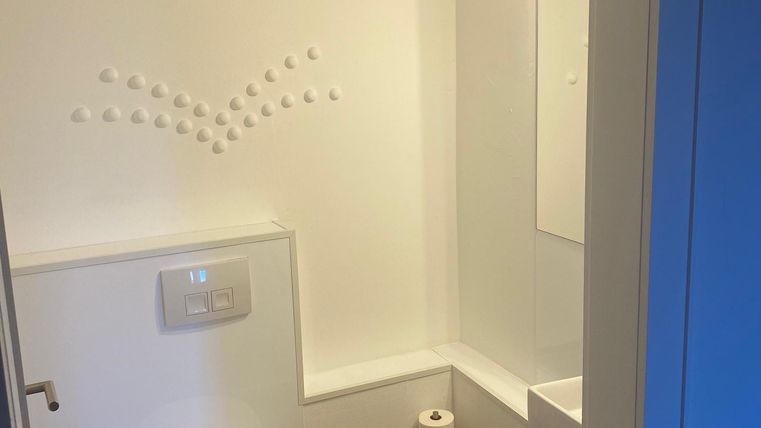 Ein modernes Badezimmer mit einer Toilette und einem kleinen Waschbecken. Die Wände sind hell und die Ausstattung ist funktional.