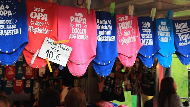 Verlaufsstand auf der Kirmes mit bunt bedruckter Babykleidung inkl. preisschild an einer Leine nebeneinander aufgehangen.