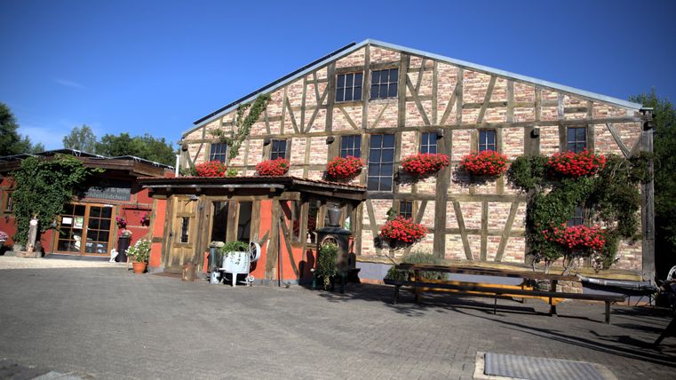 In the picture, one can see a half-timbered house that is decorated with flowers. The sun is shining and the sky is clear of clouds.