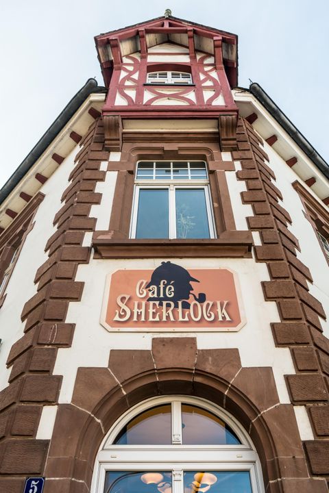 Fassade des Café Sherlock in Hillesheim mit markantem Schild und Fenster. Das Gebäude hat eine rot-weiße Fachwerkstruktur.