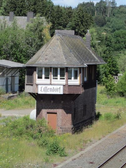 Altes Stellwerk in Lissendorf, umgeben von grüner Vegetation und Gleisen. Das Gebäude hat ein steiles Dach und ein Schild mit der Aufschrift 'Lissendorf'.