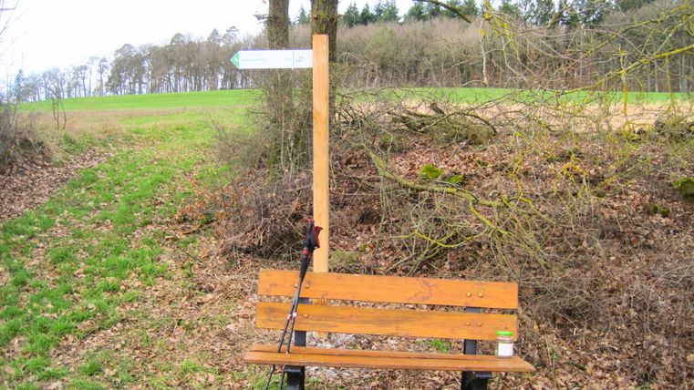 Houten bankje met wandelstok en wegwijzer in een landelijke omgeving.