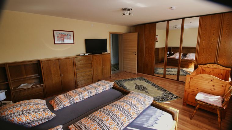 Ein gemütliches Schlafzimmer mit zwei Betten, einem Kleiderschrank und einem Fernseher. Die Einrichtung ist aus Holz und es gibt einen Teppich auf dem Boden.