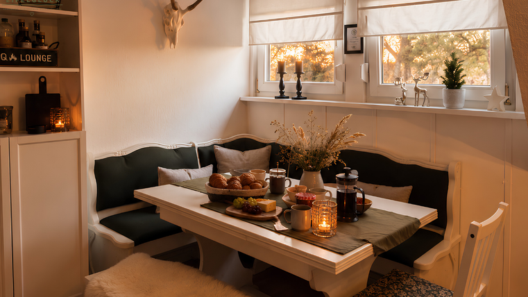 A cozy dining area with a large table and modern chairs. On the table is a flat brunch with snacks and drinks, surrounded by warm light.
