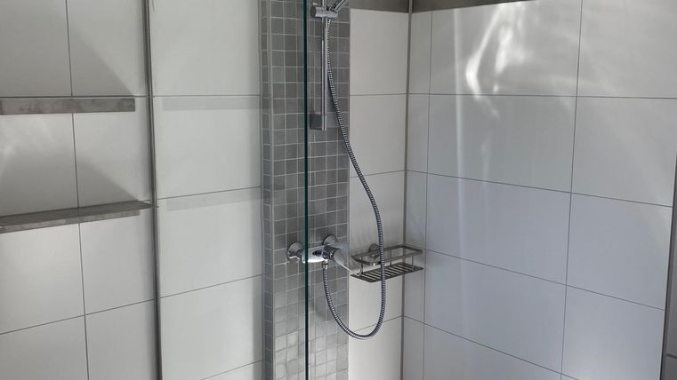 Eine moderne Duschkabine mit transparenten Glasscheiben und eleganten Fliesen. Der Raum ist hell und gut strukturiert.