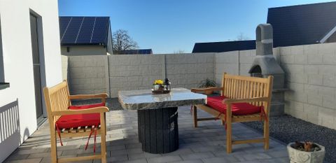 Eine hübsche Terrasse mit zwei Holzstühlen und einem Tisch aus Stein. Im Hintergrund steht ein Kamin und der Himmel ist klar.