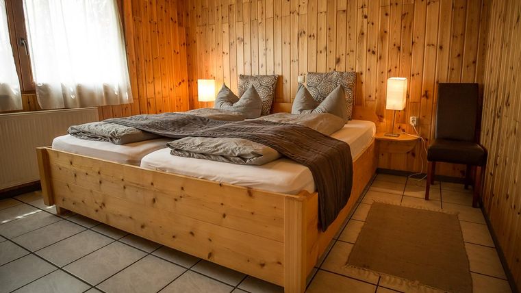 Ein gemütliches Schlafzimmer mit einem Doppelbett aus Holz und Holzverkleidung. Ein Stuhl und sanfte Lampen sorgen für eine einladende Atmosphäre.