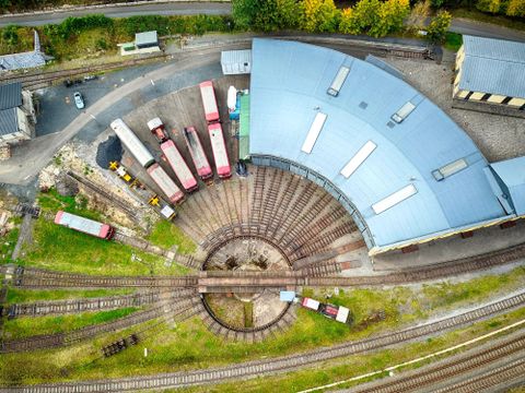 Eine Vogelperspektive auf einen Bahnhofsbereich mit mehreren Waggons und einem Dreischienengleis. Der runde Gleisabschnitt ist gut sichtbar und wird von einer großen Halle umgeben.