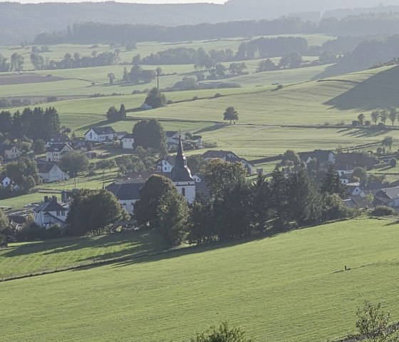 View of the village of Steffeln, surrounded by green fields and hills, with a church in the center., © Touristik GmbH Gerolsteiner Land