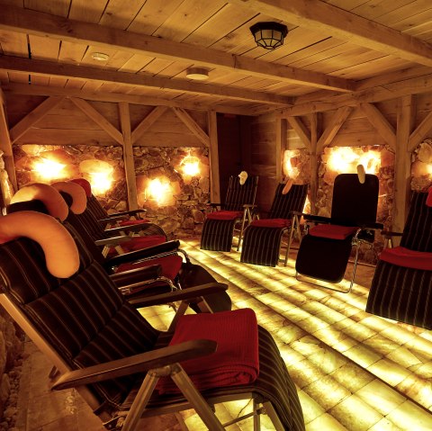  A dark room with a wooden ceiling and walls made of salt stones. There are several loungers in the room.