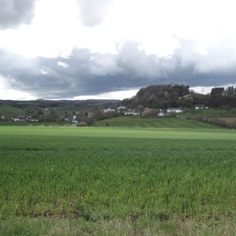 Green fields and hills under a cloudy sky, a village in the background. View towards Basberg., © Touristik GmbH Gerolsteiner Land