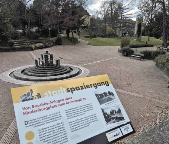 Een park met een fontein in het midden, omringd door bomen. Een bord geeft informatie over een stadswandeling van Bouch&eacute;s-Anlagen naar de Brunnenplatz., &copy; Clara Zins-Groh&eacute;
