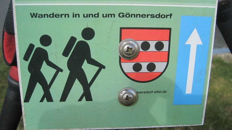 Wanderschild in Gönnersdorf mit zwei Wanderern und einem Wappen.