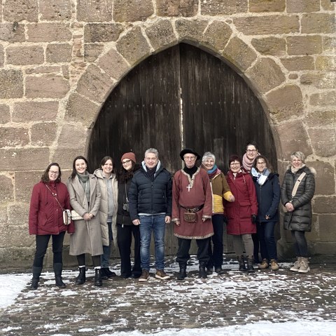 Elf Personen stehen vor einem großen Torbogen der Bertradaburg in Mürlenbach. Eine der Personen ist wie ein mittelalterlicher Knappe gekleidet.