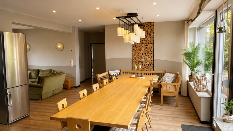 Une cuisine moderne avec une grande table en bois et des chaises en bois confortables. La pièce est bien éclairée et a de grandes fenêtres donnant sur un environnement verdoyant.