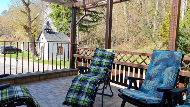 A terrace with two lounge chairs and a beautiful view of nature. In the background, there is a small building and trees visible.