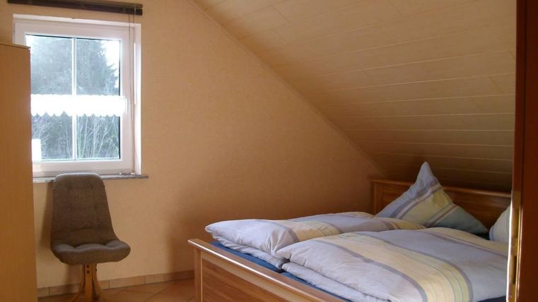 Ein gemütliches Schlafzimmer mit schrägen Wänden. Es enthält ein Bett, einen Stuhl und ein Fenster mit Blick nach draußen.