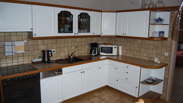 A modern kitchen with white cabinets and wooden details. It is well equipped with appliances such as a microwave and a kettle.