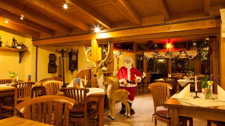 Ein gemütliches Restaurant mit Holzdekor, das festlich geschmückt ist. Im Vordergrund steht ein Weihnachtsmann neben einem Reh.