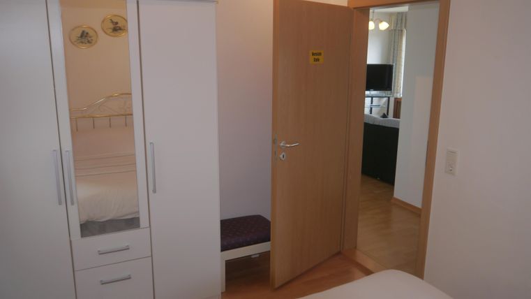 Ein Innenraum mit einer geöffneten Tür und einem Kleiderschrank. Im Hintergrund ist ein weiterer Raum mit einem Fernseher sichtbar.