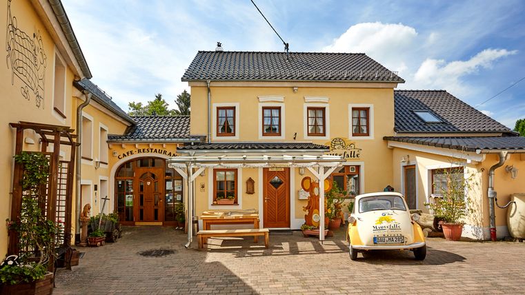 Ein gelbes Café mit dem Namen 'Mausefalle', ein kleines Auto steht davor.