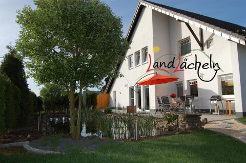 Ein modernes Haus mit einem schönen Garten und einer Terrasse. Der große Baum und die bepflanzte Umgebung schaffen eine einladende Atmosphäre.