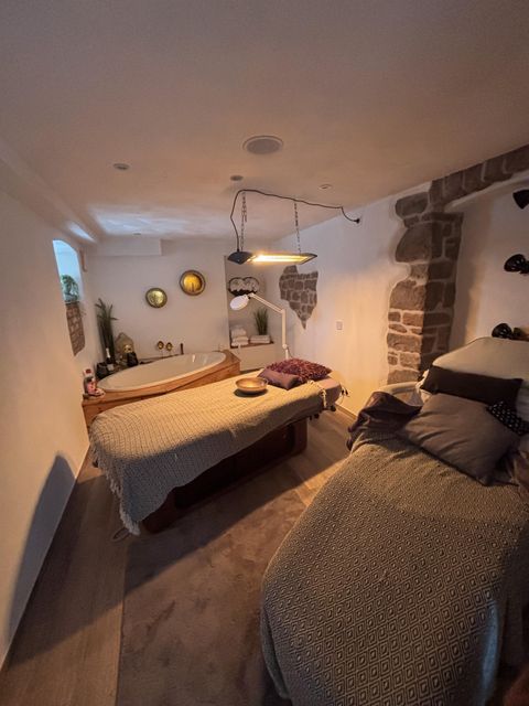 Une pièce confortable avec de grands tables de massage et une atmosphère relaxante. Les murs sont partiellement revêtus de pierres naturelles et il y a des éléments décoratifs.