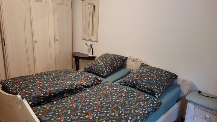 Une chambre lumineuse avec un lit double et des housses de couette colorées. À côté du lit se trouve une table de chevet et une armoire est visible en arrière-plan.