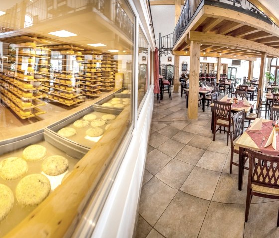 A large glass front, behind which numerous cheese wheels mature on shelves and in basins. On the other side is a restaurant.
