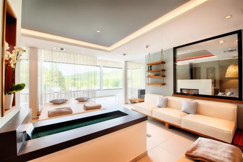 Modernes Spa mit hellen Möbeln, Liegen, einem Wasserbecken und großen Fenstern mit Blick ins Grüne.