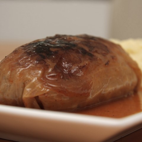 A cabbage roll in a baking dish with sauce and mashed potatoes on the side.