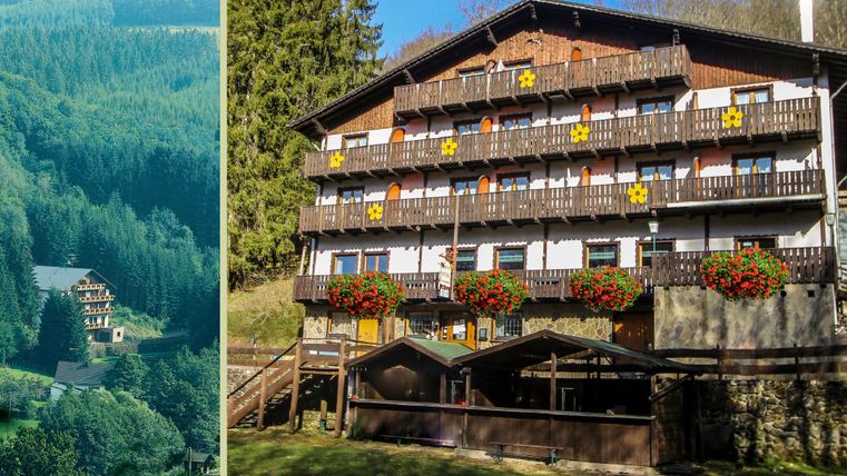 Un hôtel confortable dans la verdure avec des balcons et des jardinières fleuries. En arrière-plan, des collines boisées sont visibles.