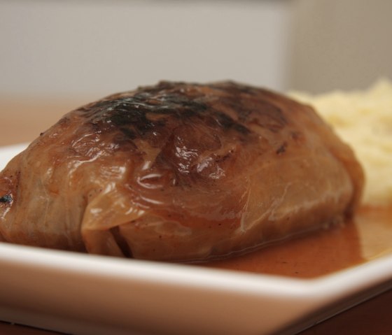 Eine Kohlroulade in einer Backform mit Sauce und Kartoffelpürree daneben