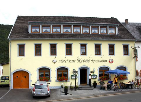 Ein charmantes Hotel mit dem Namen "Hotel zur Krone" in einem gelben Gebäude. Vor dem Hotel gibt es einen Außenbereich mit Tischen und Stühlen sowie einige Fahrräder.