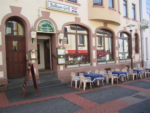 Außenansicht eines Restaurants mit kroatischen Spezialitäten. Tische mit blauen Tischdecken und Stühlen stehen auf dem Gehweg bereit.