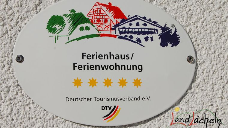 Ein Schild für ein Ferienhaus mit fünf Sternen. Es enthält den Namen der Unterkunft und das Logo des Deutschen Tourismusverbands.