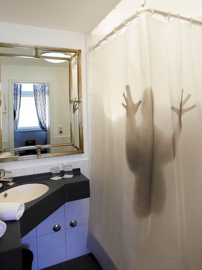 Une salle de bain avec un miroir, un lavabo et des serviettes. Dans le rideau de douche, on peut voir l'ombre d'une personne qui pousse ses mains contre le rideau.