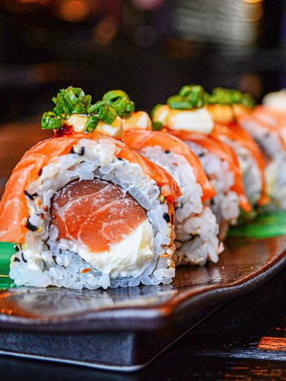 Sushi-Rollen mit Lachs, Frischkäse und Frühlingszwiebeln auf einem Teller, Nahaufnahme.