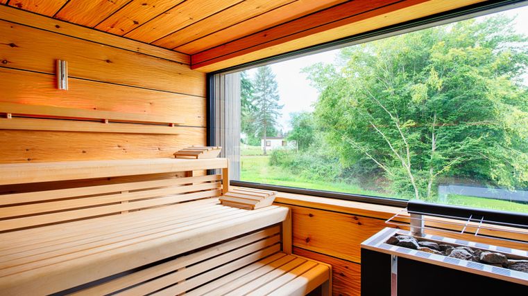 Eine moderne Sauna mit Holzverkleidung und großen Fenstern. Der Blick zeigt einen grünen Garten im Freien.