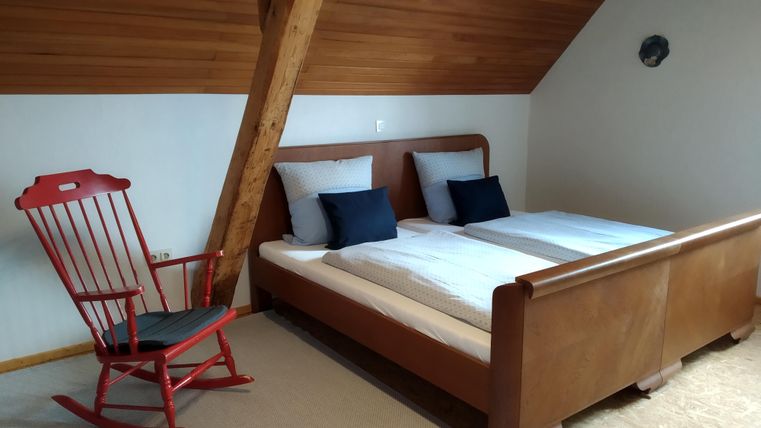 Une chambre confortable avec un lit double et des coussins décoratifs. À côté du lit, il y a un rocking-chair en bois rouge.