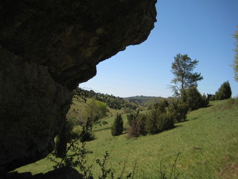 Blick durch einen Felsvorsprung auf eine grüne Hügellandschaft mit Bäumen und blauem Himmel.